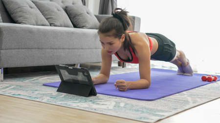 Young muscular fitness woman doing Planking exercising on yoga mat at home on living room floor