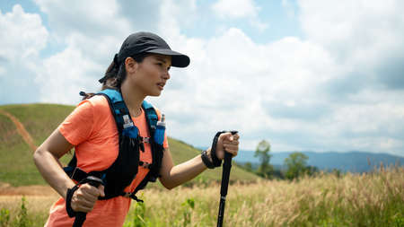 Young women active trail running across a meadow on a grassy trail high in the mountains in the afternoon with trekking poleの写真素材