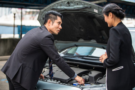 Businessman helping to check and fix a broken woman's car on the side of the roadの写真素材