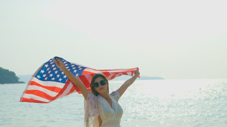 young women hold American flags on the beach and the sea on their summer vacation and they smile and enjoy their vacation.の写真素材