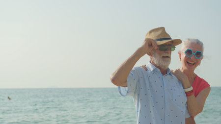 An elderly couple hugs their shoulders at the beach on their summer vacation and they smile and enjoy their vacation.の写真素材