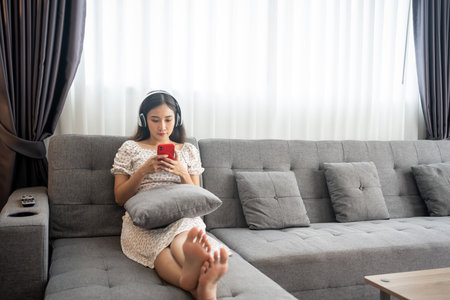 Woman wearing headphones and listening to music and singing happy at home on vacationand happy on the sofa in the living roomの写真素材
