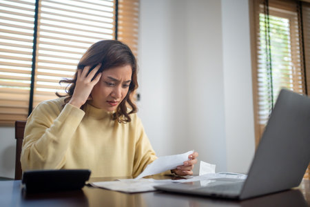 A woman uses a calculator to check the sum of her home expenses and she is stressed over the home...