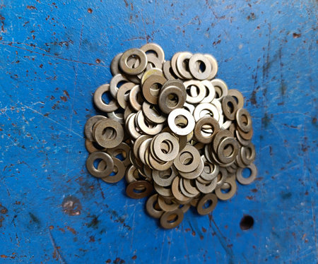 A close-up, high-angle photograph showcasing a circular mound of small metal flat washers (plain...