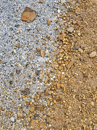 A high-angle, top-down view of a textured ground surface showing a distinct transition between two soil types. The left side features loose, grey and white granite gravel, while the right side shifts to rich yellow, ochre, and rusty-brown clay earth.の写真素材