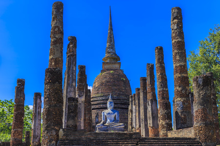 Ancient Buddha statue and pagodas against blue sky at Sukhothai Historical Park, Thailandの写真素材