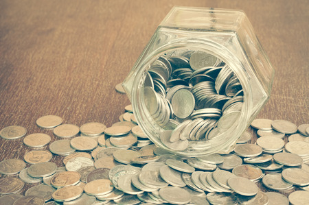 Coins spilling out of a glass bottle with filter effect retro vintage styleの写真素材