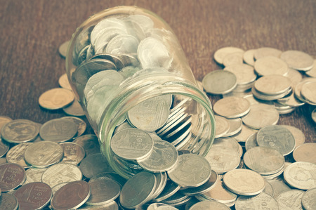 Coins spilling out of a glass bottle with filter effect retro vintage styleの写真素材