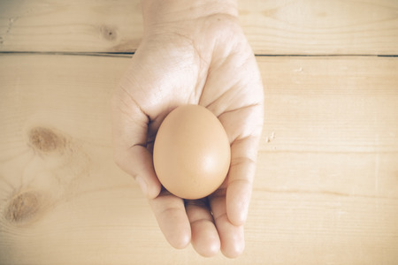 hand holding egg on wooden background with filter effect retro vintage styleの写真素材