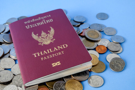 Thailand passport  brown cover and money coin on blue paper background for traveling on holidaysの写真素材