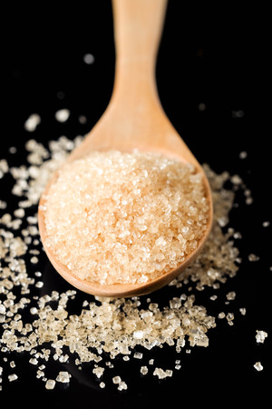 Brown sugar in wood spoon on black background.Components of The food is sweet delicious.