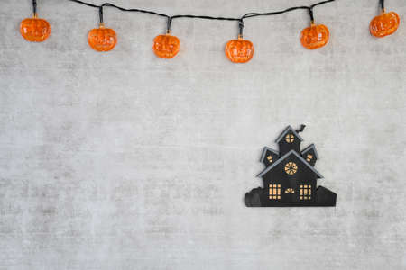 Halloween background with plastic small orange pumpkin light and small wood black house on white...