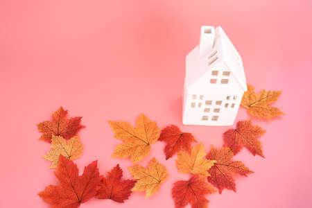 Automne background with  colorful of autumn ' s leaves  and small ceramic white house on  pink background and space for write text , decorate  or inviting halloween concept.の写真素材