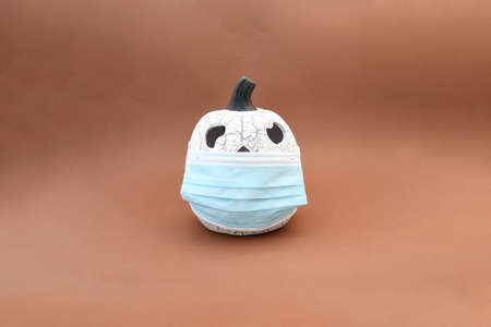 Object, ceramic pumpkin wearing a protective medical mask on brown background. Infor for autumn...