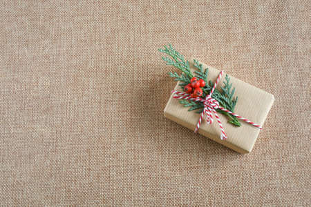 Close up present box with green leaf of pines and branche of small red fruit on brown tissue with space for text, decorate on christmast concept.の写真素材