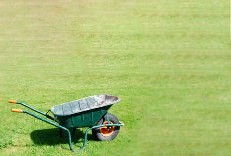 Old green empty wheelbarrow on green yard garden with space fort text vintage object
