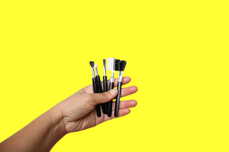 Selective focus, woman asian hand holding cosmetic tools on yellow background and clipping path.