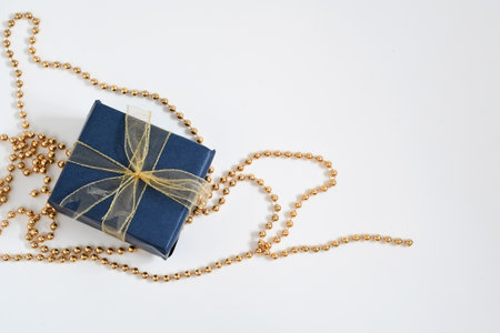 Christmas gift box wrap with blue navy paper and golden ribbon on golden necklace on white background with space for text. Handmade objects , Christmas holiday concept.の写真素材