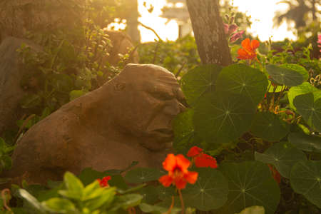 Ogre statue in a garden. Rustic sculpture of an ogre in the undergrowth of a garden. The sun sneaks...