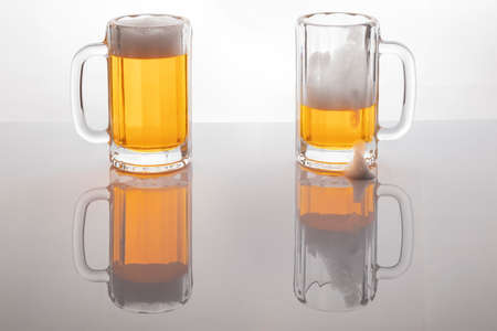 Beer mugs with beer. Beer without frosting. Beer mugs on white backlit background. One glass almost empty and one full.の写真素材