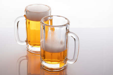 Beer mugs with beer. Beer without frosting. Beer mugs on white backlit background. One glass almost empty and one full.の写真素材