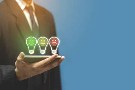 A business man standing with a smartphone with a happy smile icon Customer service evaluation conceptの写真素材