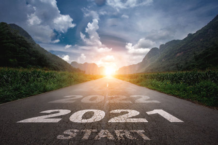 2021, The New Year 2021 or the beginning of the concept of the word 2021 is written on the road in the middle of the asphalt road with a sunset mountain backdrop, concepts of planning and challengesの写真素材