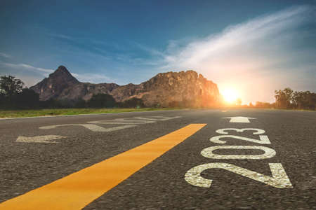 2023 new year 2023 or beginning of 2023 word concept written on a road in the middle of a country road with mountains sunset concept backdrop.の写真素材