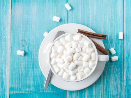 A cup of hot cocoa with marshmallows and sticks of cinnamon on a bright blue wooden background shabby.の写真素材
