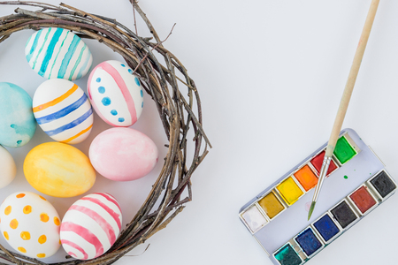 Colorful Easter Eggs isolated on the white background with nest and wreath and watercolor paint and brush. Selective focusの写真素材