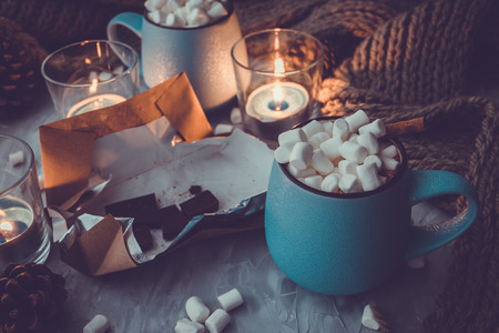 Christmas and New Year cozy holiday composition with cinnamon, candles, scarf, chocolate, pine cone, mugs with cocoa or chocolate, marshmallow on the gray concrete background.の写真素材