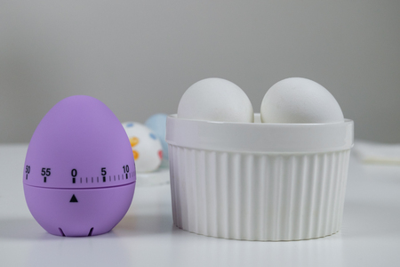 A table with white and colored eggs and violet kitchen timer, prepared for decoration for Easter.の写真素材
