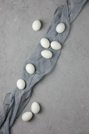 White chicken eggs with gray gauze on a gray concrete background. Top view. Flat lay. Postcard for Easter and Spring Holidays.の写真素材