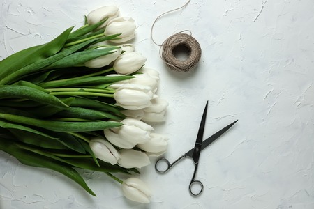 A bouquet of white tulips on a white concrete background with twine and scissors. Top view. Flat lay. Postcard for Easter, Mothers Day and Spring Holidays.の写真素材