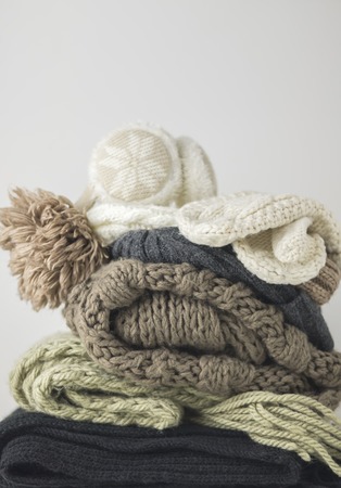 Warm woolen knitted winter and autumn clothes, folded in a pile on a white table. Sweaters, scarves,...