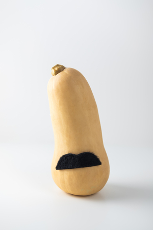 Brightly orange pumpkin with black mustache on light white background. Concept of Halloween, autumn festivals, World month of prostate cancer.の写真素材