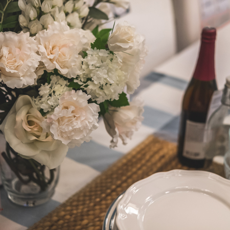 Close-up table setting. On the table are plates on napkin, bottle of wine and vase of flowersの写真素材