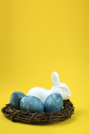 Easter nest with blue eggs and white rabbit on a yellowの写真素材