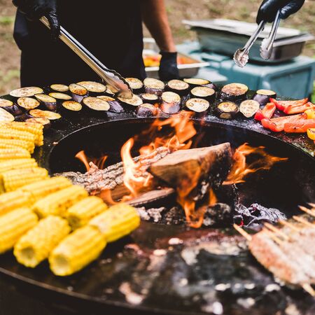 Round barbecue grill with open fire inside. Meals for the summer picnic are being prepared: corn,...