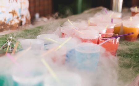 Steaming multi-colored cocktails with dry ice standing on green background.の写真素材