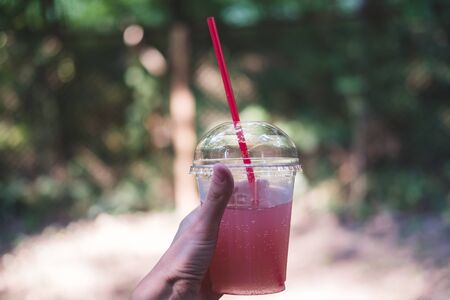 Glass of pink lemonade on hot summer day. Female hand holds plastic glass with straw.の写真素材