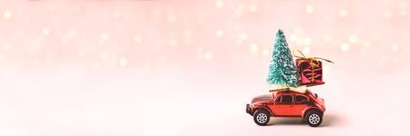 Toy car with Christmas tree and gift on roof. Background of blurred bokeh from garland. New Year and...