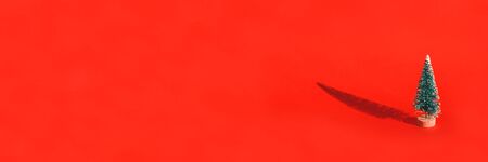 Miniature toy artificial Pine tree on wooden base on bright red Christmas background with long...
