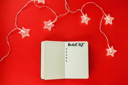 Notebook for wish list, goals or promises for New Year on red background and garland in form of...