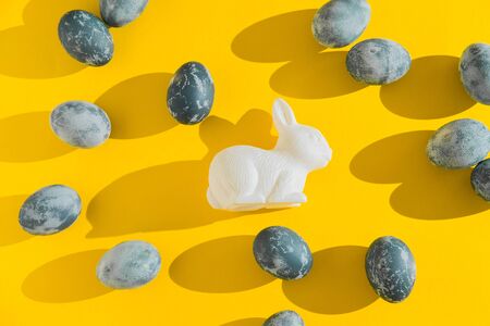 Blue textured colored Easter eggs and white plactic bunny on a bright yellow holiday background...