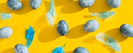 Blue textured colored Easter eggs and chicken bird feathers on a bright yellow holiday background backdrop. Spring holiday concept. Copyspace. Flat lay. Top view. Hard light. Long shadowの写真素材