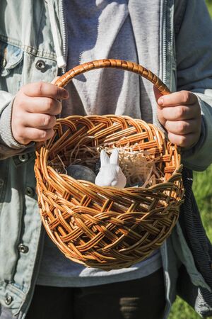 Childrens teenage hands hold a wicker brown hand-made basket with blue textured Easter eggs and a...