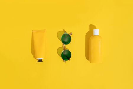 Summer bright flatlay on colorful background with tubes and bottle with sunscreen, green sunglasses....