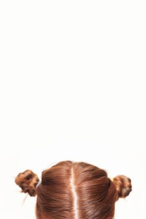 Head of a girl with two messy twisted curled red hair buns on whiteの写真素材