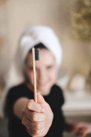 Young beautiful girl with towel on her head after shower, in bathroom holds bamboo eco toothbrush in front of her. The concept of sustainable morning oral and dental care.の写真素材